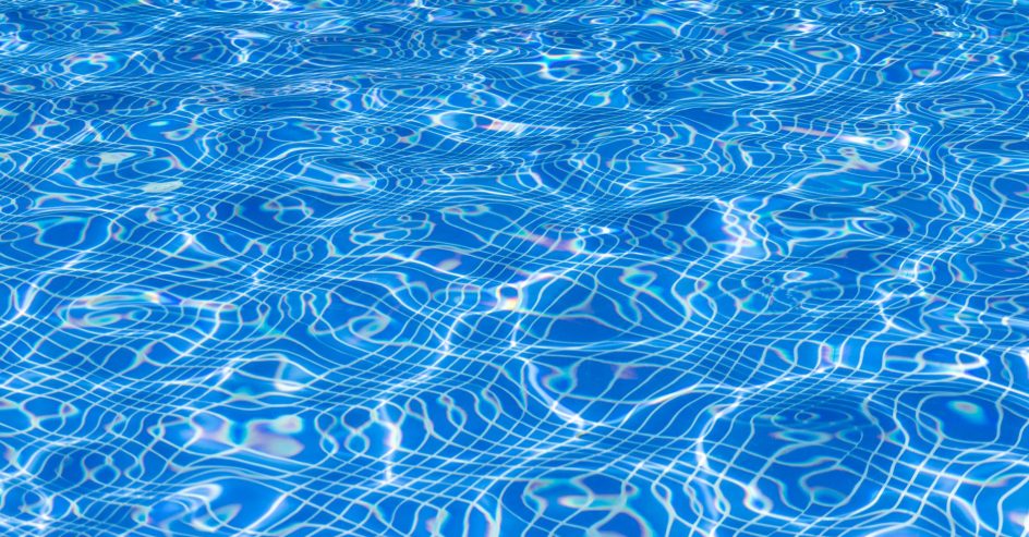 Sunlight rippling over clear pool water above a blue tile surface