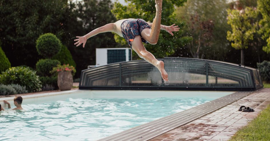 Swimmer diving into a backyard pool with a heat pump unit and a low pool enclosure behind it