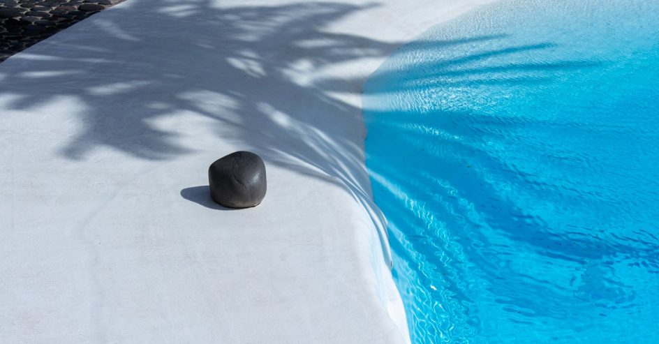 Smooth white plaster pool edge curving into clear blue water, with palm shadows across the finish