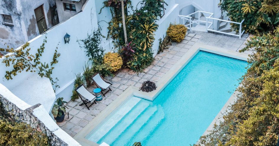 Overhead view of a walled courtyard pool with pale stone coping, lounge chairs, and tropical plants