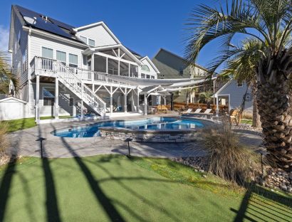 Backyard pool with a raised stone-wall spa behind a raised coastal home, framed by a palm tree
