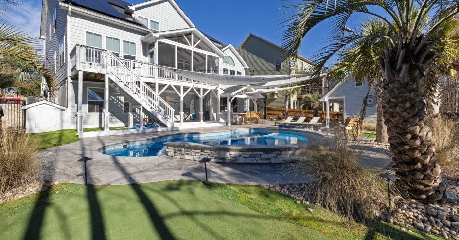 Backyard pool with a raised stone-wall spa behind a raised coastal home, framed by a palm tree